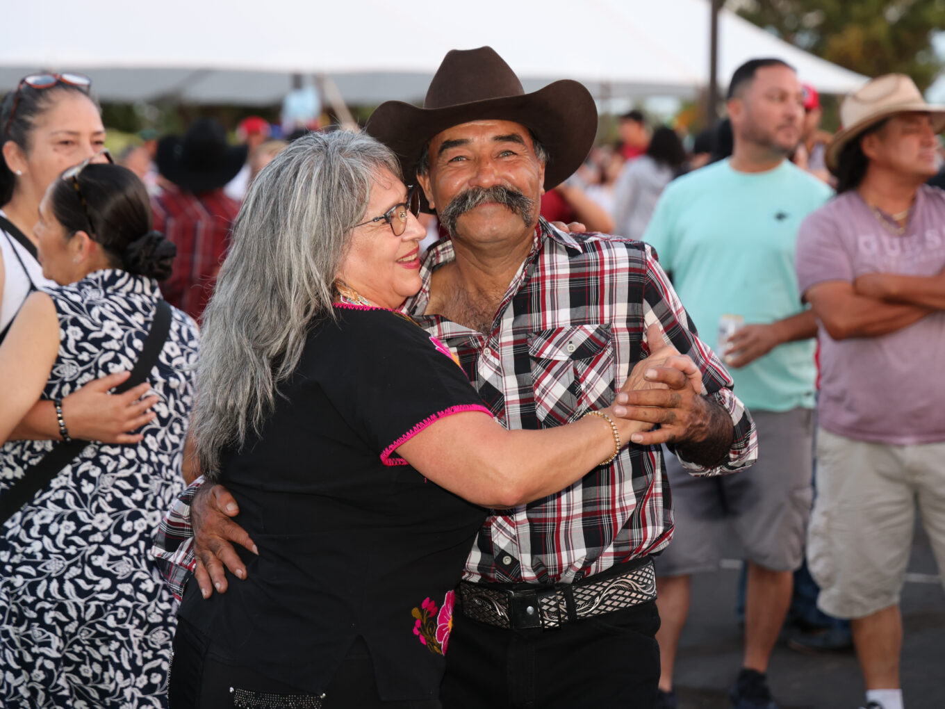 Couple dancing joyfully at an outdoor event with others in the background