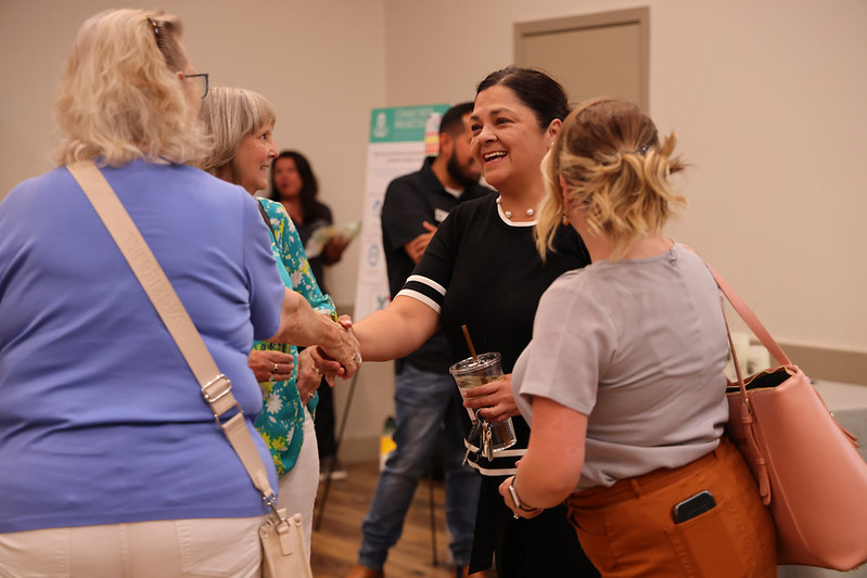 54395123930_1cde2c028b_c.jpg smiling woman shaking hands with another woman in a lively social gathering