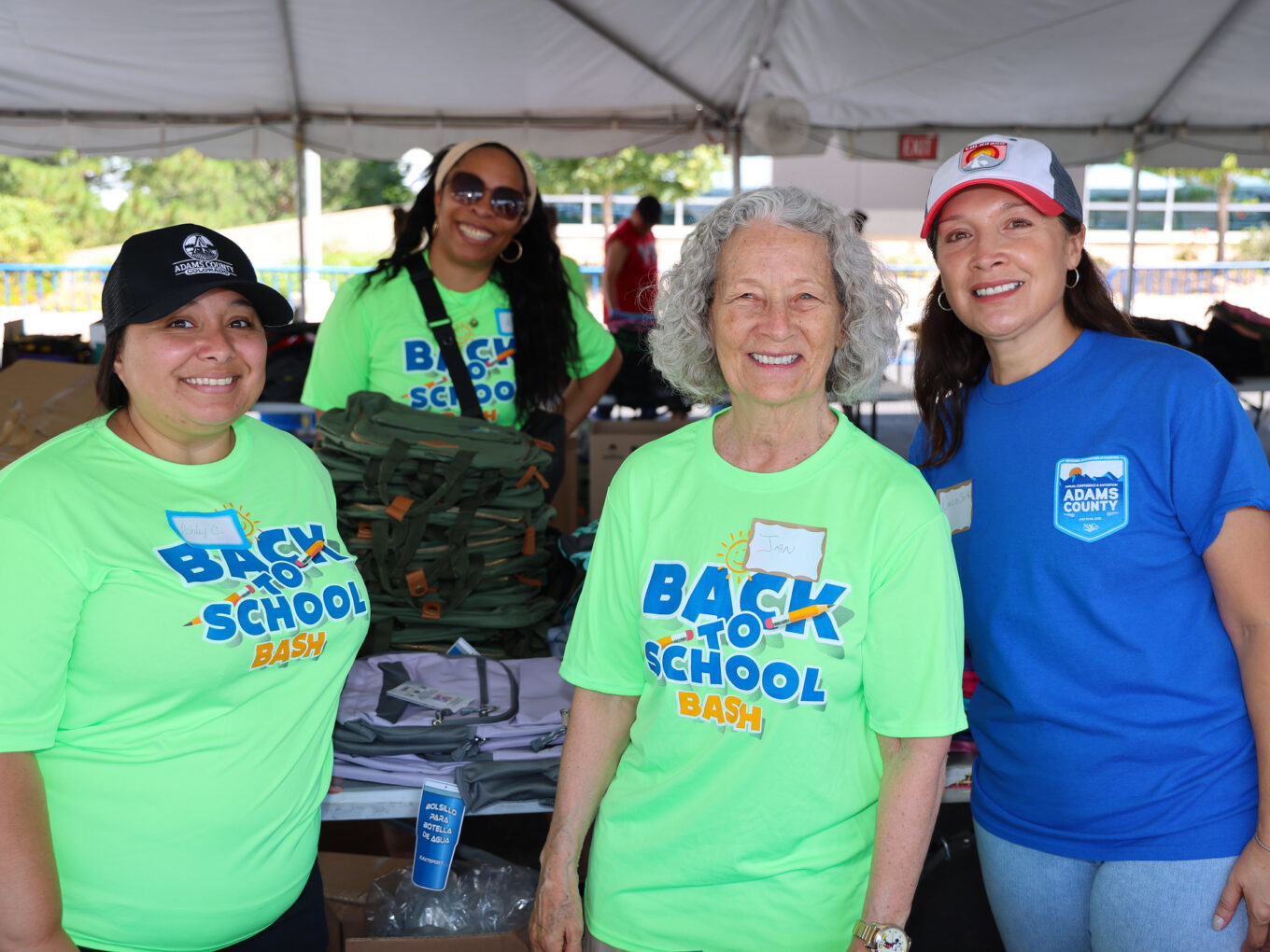 Four women smiling at a "Back to School Bash" event, organizing backpacks.