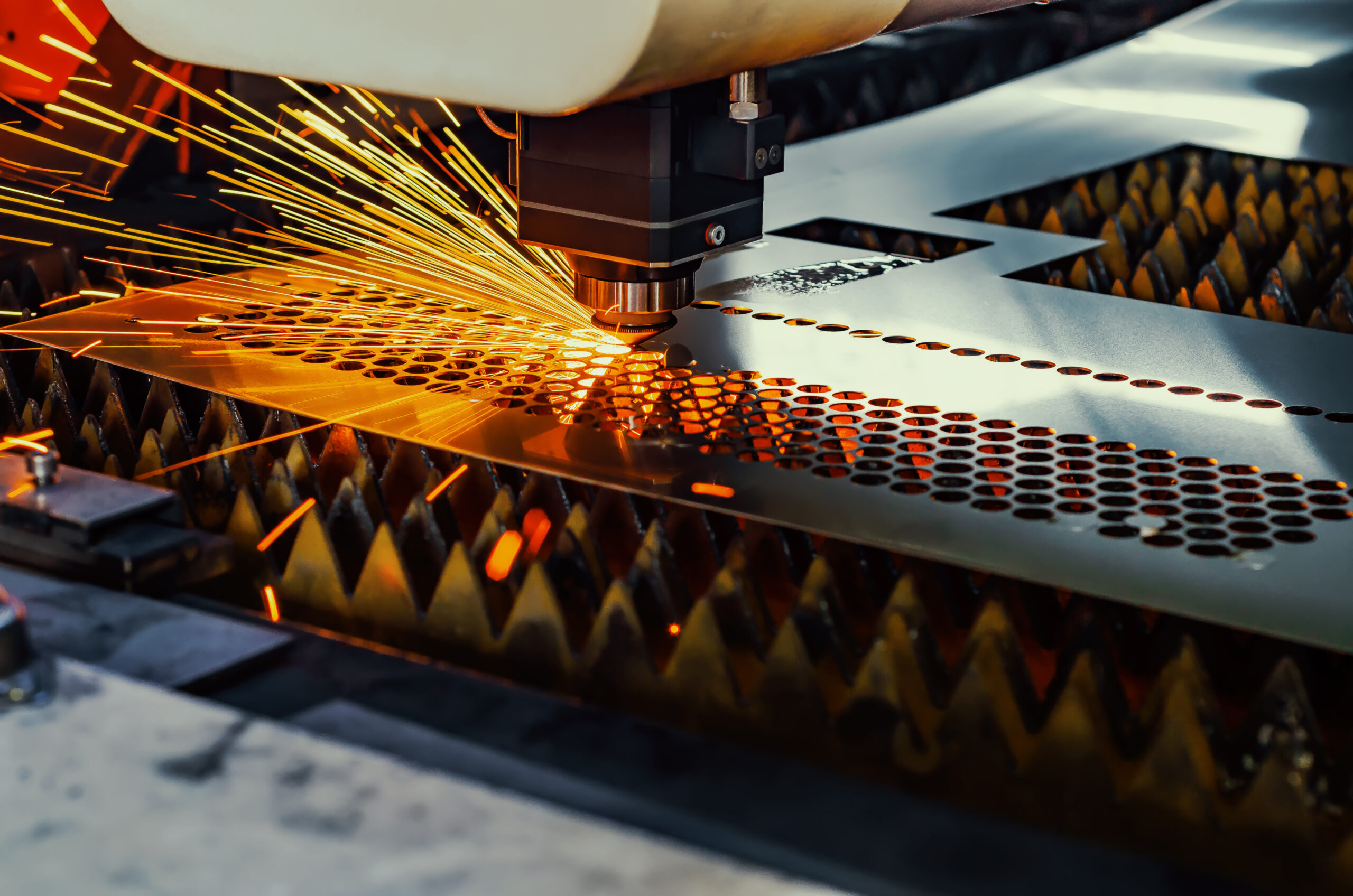 Laser cutting machine emitting sparks, creating precise circular patterns on metal sheet.