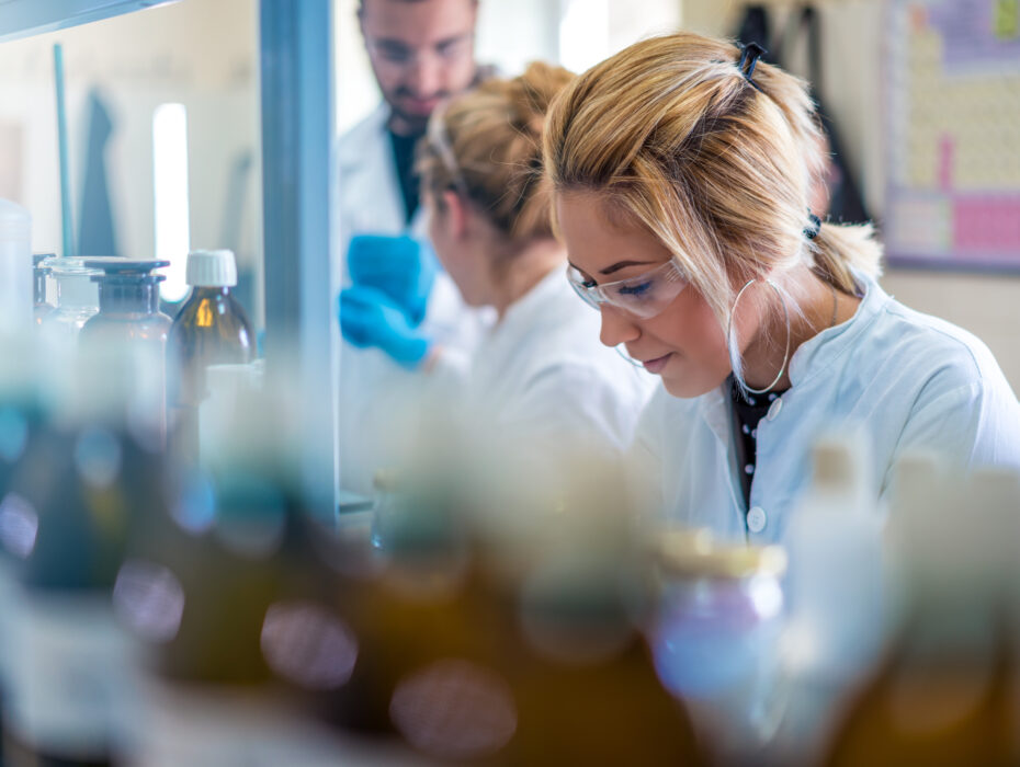 Young female scientist in a lab, focused and wearing safety goggles