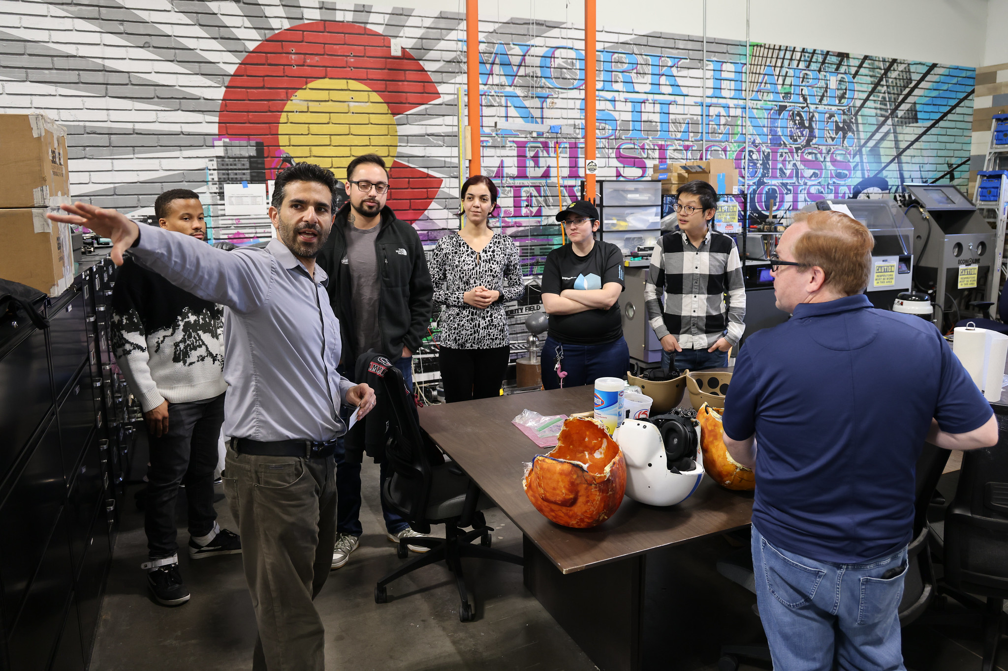 Man leading discussion with group in workshop, mural reads "Work Hard in Silence Let Success Make Noise"