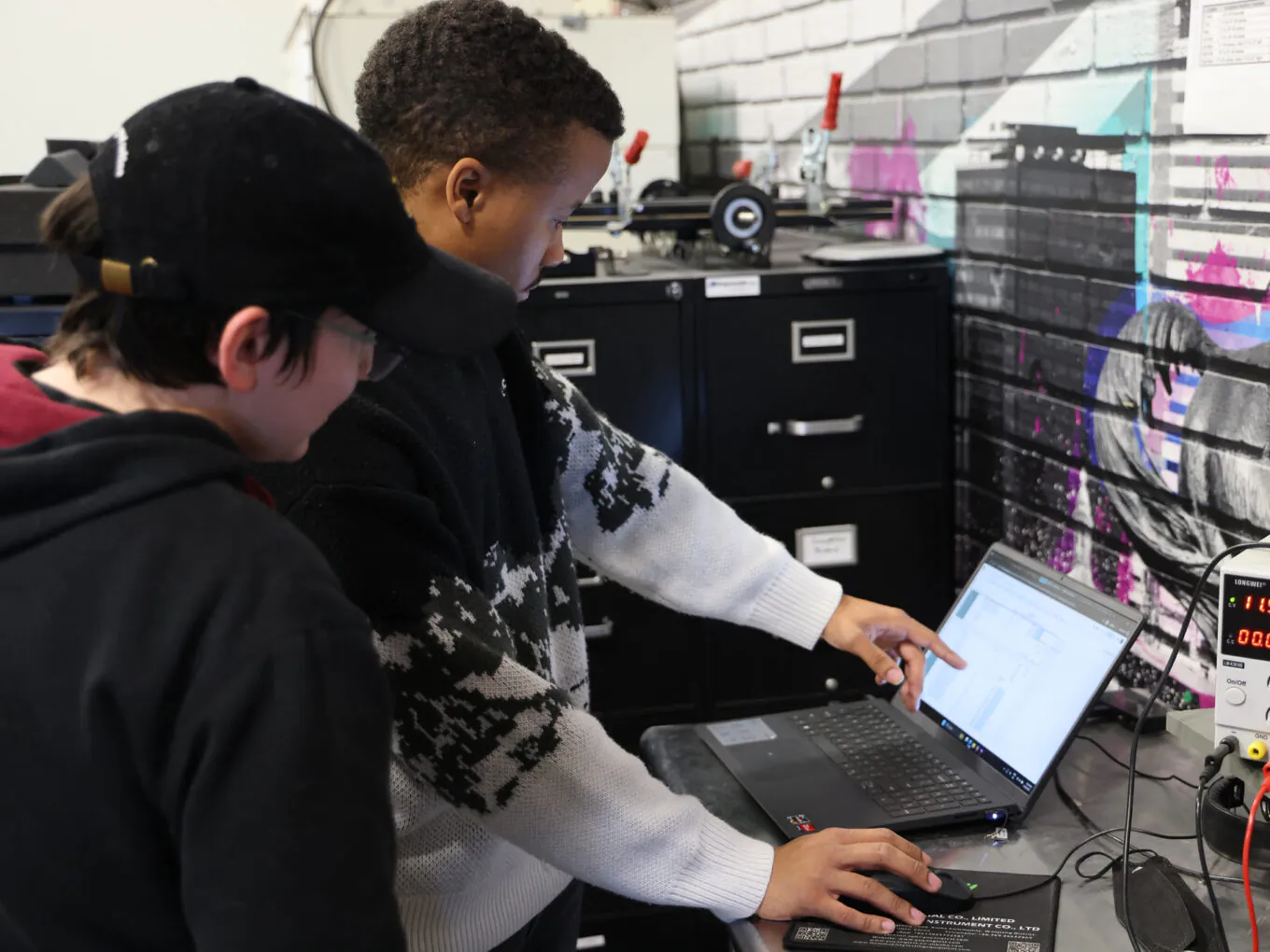 Two people collaborating at a laptop in an industrial workspace.