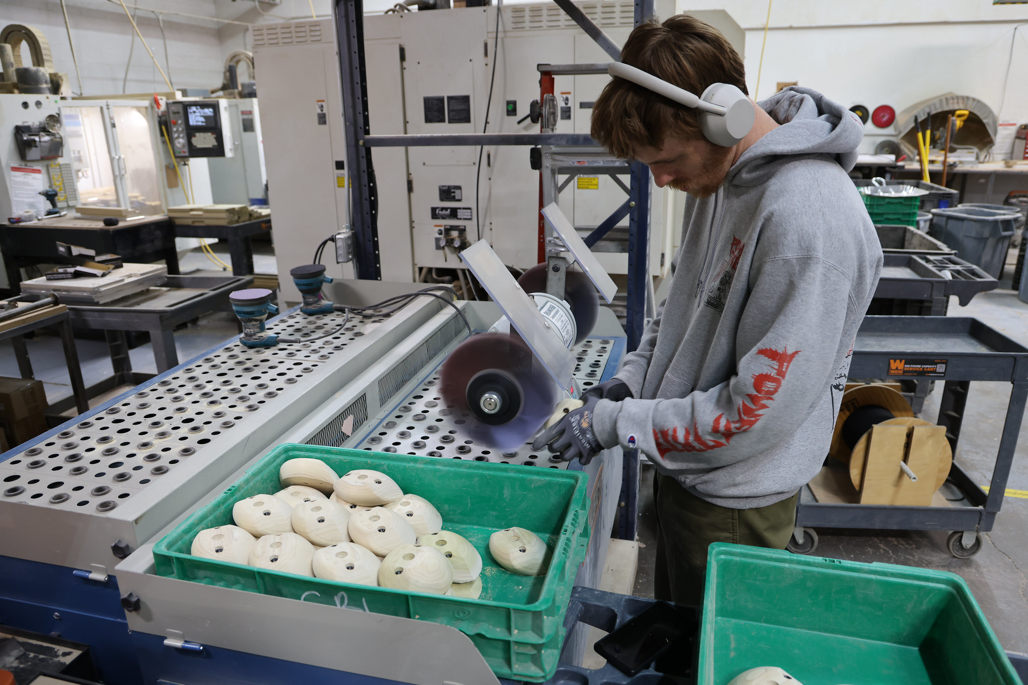 Person sanding wooden pieces in a workshop, wearing headphones.