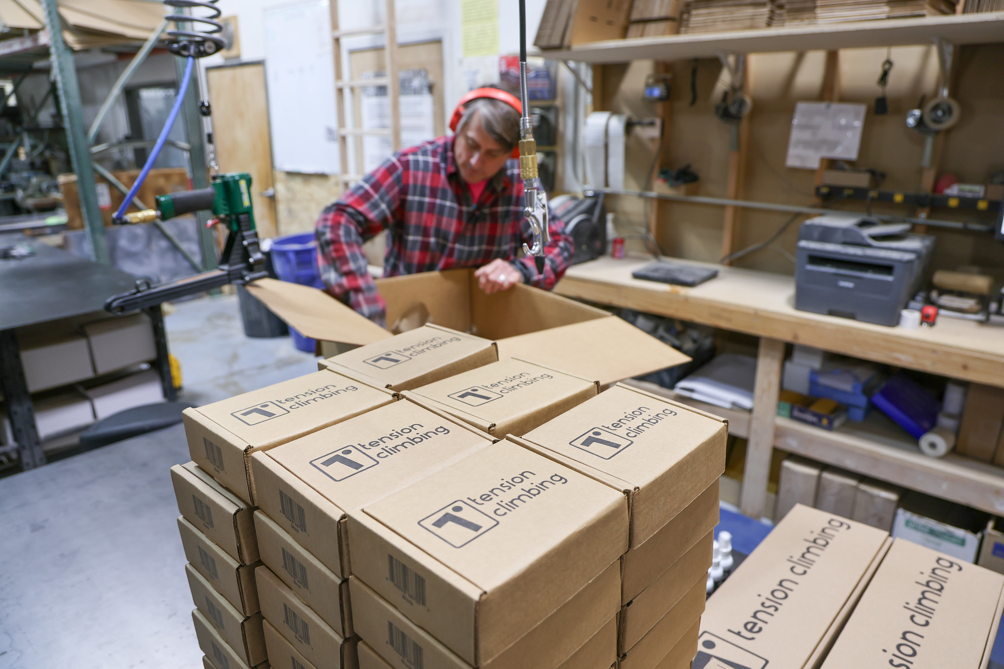Worker in plaid shirt packing Tension Climbing boxes in warehouse.