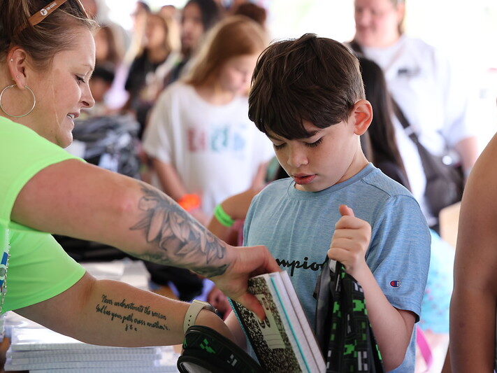 Child receives school supplies from a volunteer with tattooed arm.