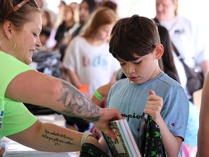 Child receives school supplies from a volunteer with tattooed arm.