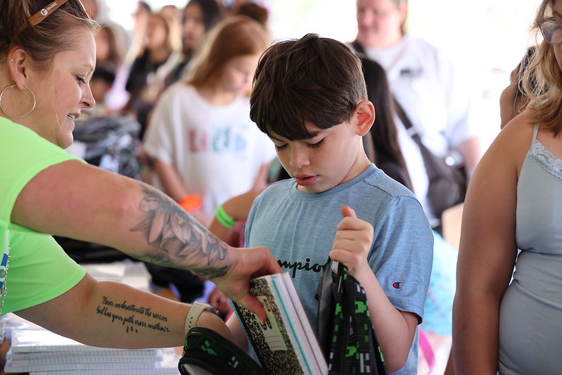 Child receives school supplies from a volunteer with tattooed arm.