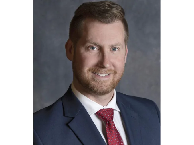 Bill Aiken smiling, wearing a suit with a red tie.