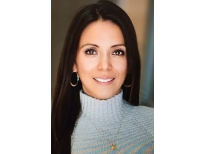 Delia Sánchez smiling with long hair, wearing a light sweater and hoop earrings