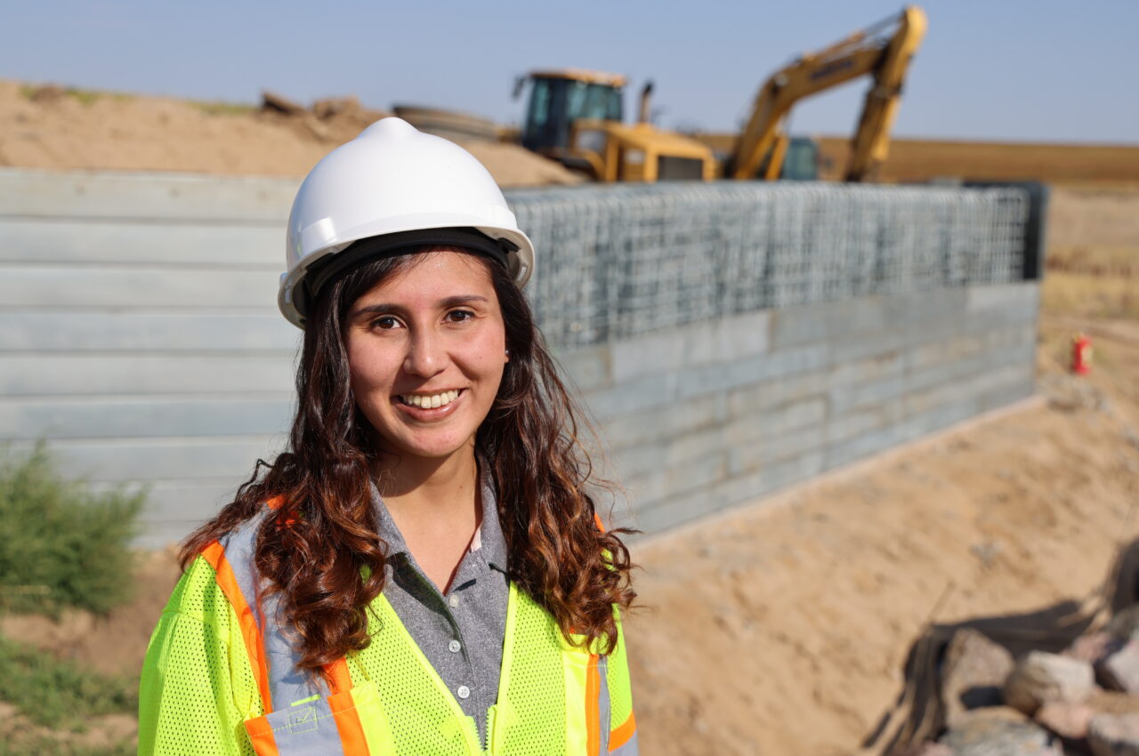 Smiling construction worker in hard hat and safety vest at site with heavy machinery.